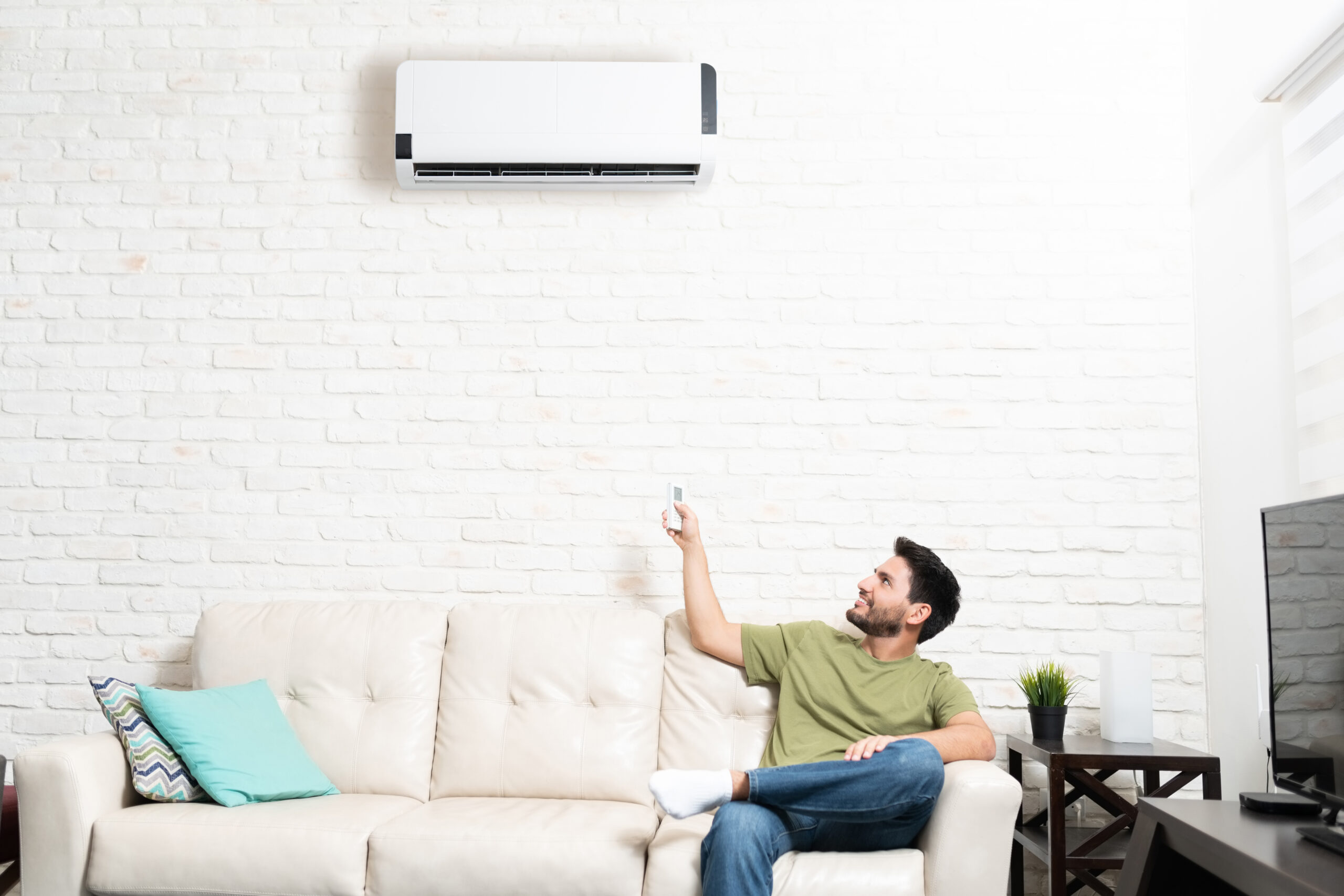 Latin Man Adjusting Temperature Of Mini Split At Home Man enjoying cool air from a mini split system after electrical panel upgrade in San Diego home